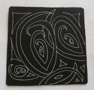 A black Zentangle tile with white Zentangles