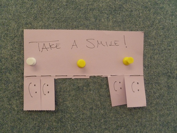 Paper smiles for the taking, outside a cubicle