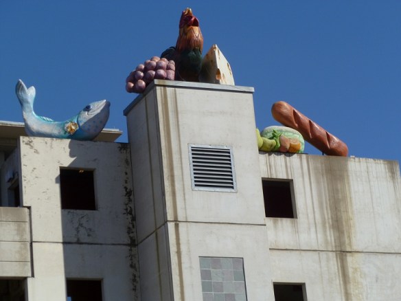 A parking garage topped with a giant fish, chicken, and a loaf of French Bread