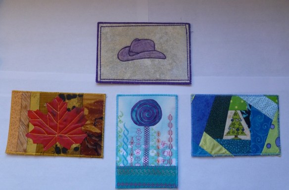 Four fabric postcards: a purple cowboy hat, a red maple leaf, a fantasy tree with decorative stitching and a Christmas tree