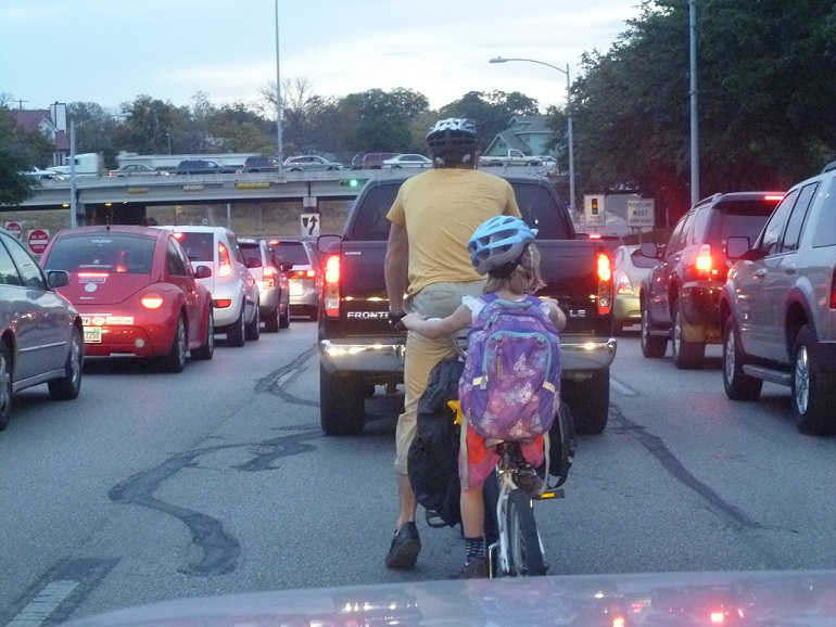A father and daughter on a bicycle in traffic