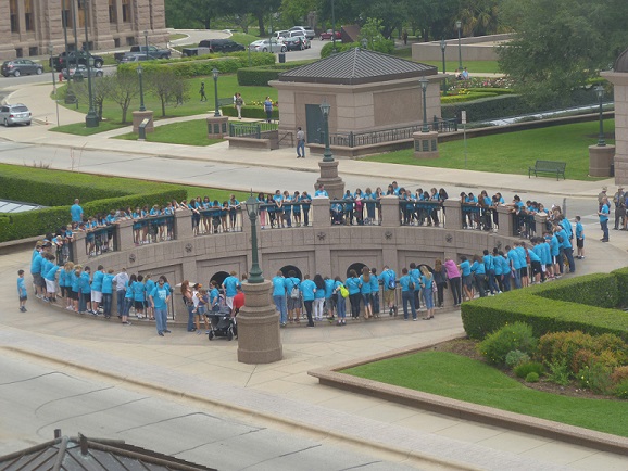 Lots of people in blue t-shirts looking over a railing, in a circle