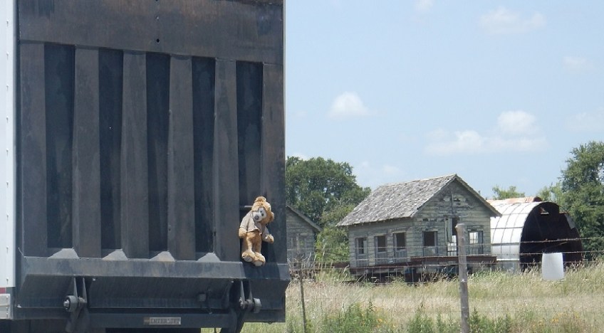 A stuffed animal bear attached to the back of a delivery truck.