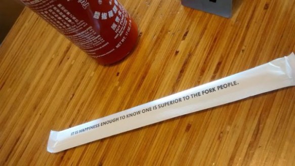 Friday Fictioneers photo prompt.  Chopsticks in a paper sheath with the words: It is happiness enough to know one is superior to the fork people