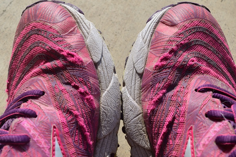 Pink running shoes that have holes worn through the tops