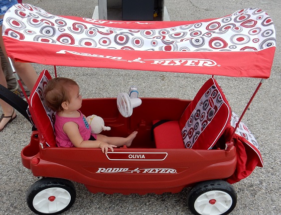 A Radio Flyer wagon with a canopy and a fan with a little girl sitting in it. 