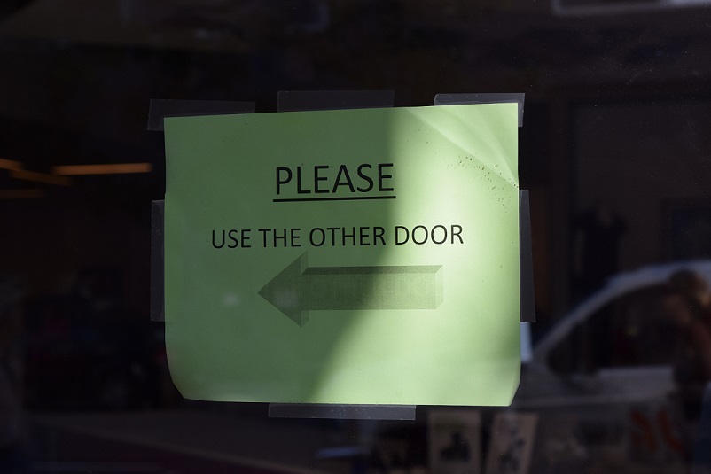 Sign on door that says "Please use the other door" and it has an arrow pointing to the left