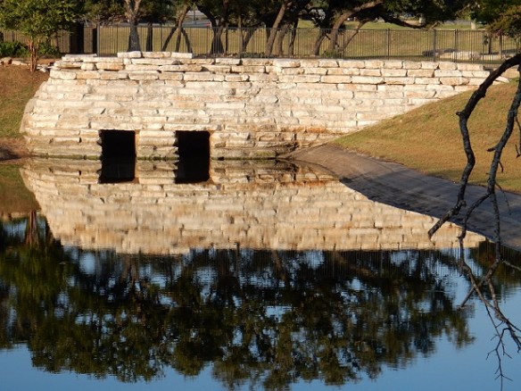 Trees reflected in the water over a stone walking bridge