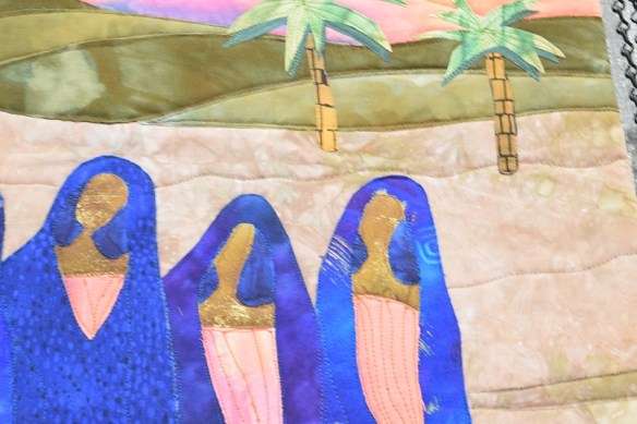 A close up of the art quilt Blue Women by Dee Merrill, showing the blue robes against the desert sand