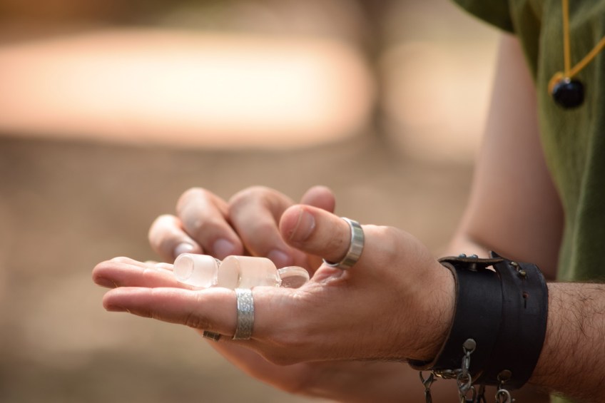Two hands, one hand with two rings (one on thumb, one on forefinger) with translucent glass objects in the palm