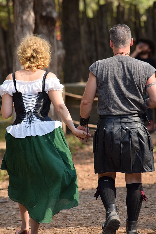 Two people dressed in Celtic clothes, walking hand in hand, seen from the back