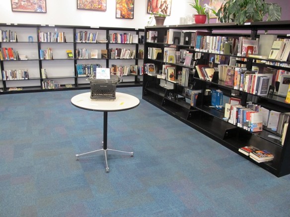 A small round table with a manual typewriter on it. The sign on the typewriter says "NaNoWriMo Write-In Space"
