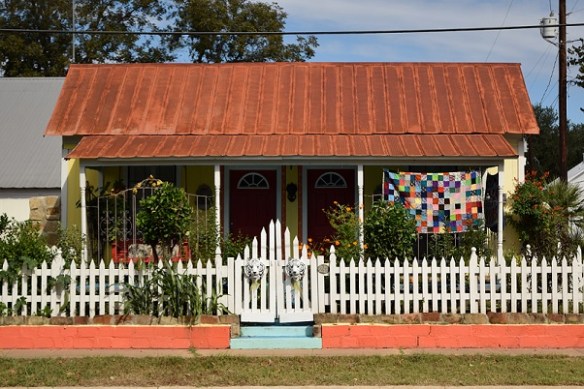A cute cottage with a colorful quilt hanging in front of it
