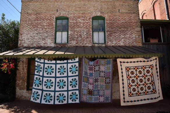 Three old quilts hanging in front of an old building