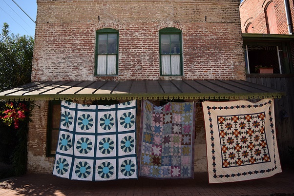 Three old quilts hanging in front of an old building