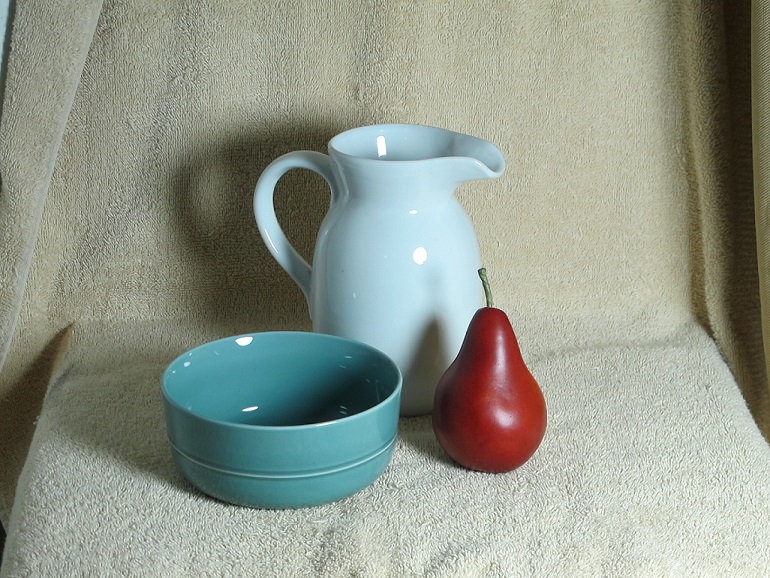 The trio of objects for my charcoal sketch: a blue ceramic bowl, a pear and a white pitcher