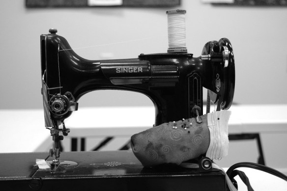 An old Singer sewing machine in a black and white photo.  The caption is "Sally sews pillow shams on her Singer down by the seashore"