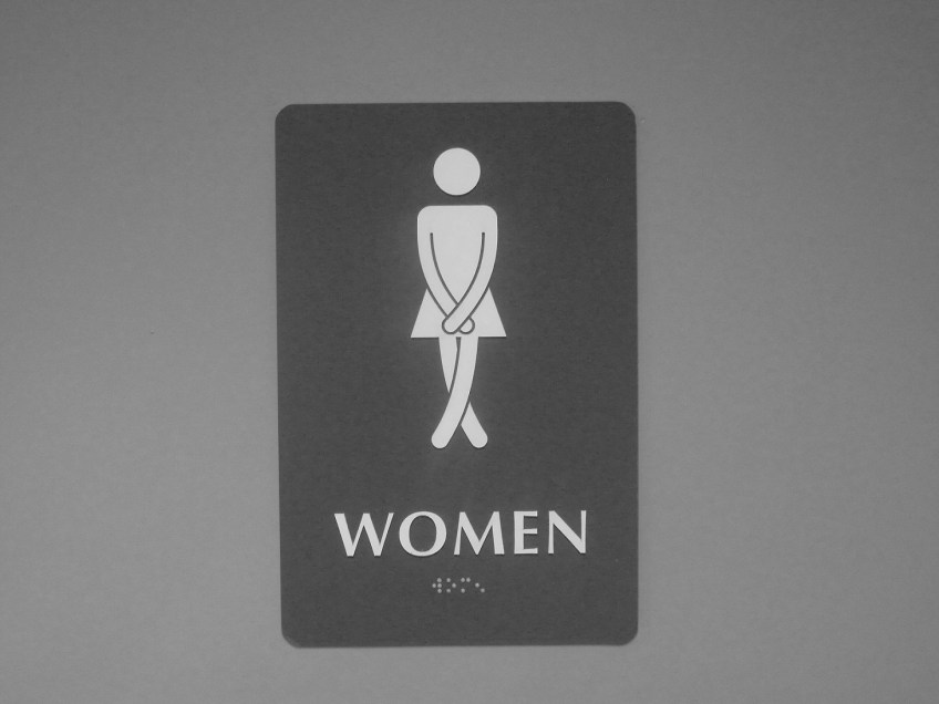 Sign to a women's bathroom with the image of a woman crossing her legs, trying not to go to the bathroom before she gets inside